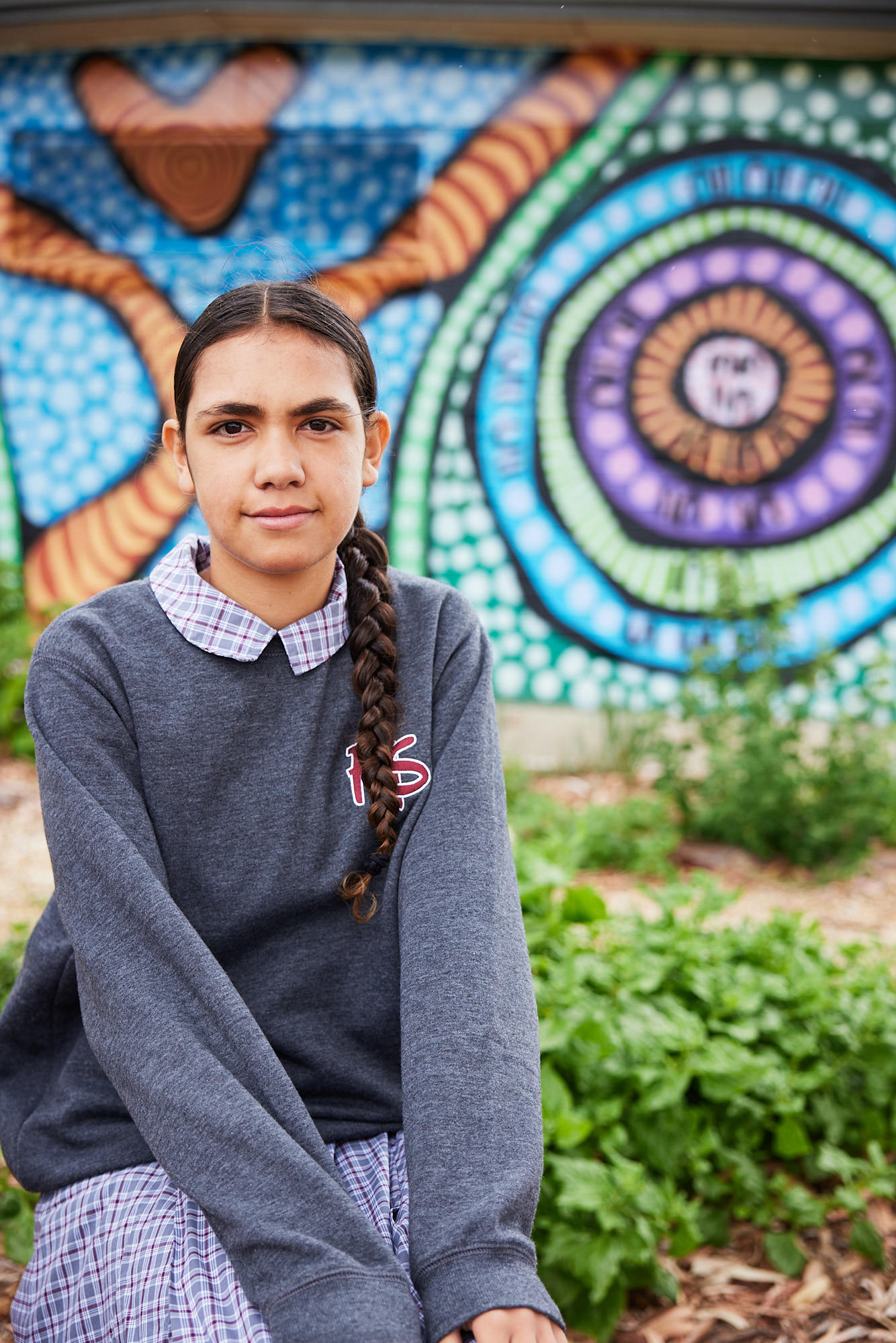 Student sitting and smiling in the Yarning circle with colourful Aboriginal artwork painted on building in the background